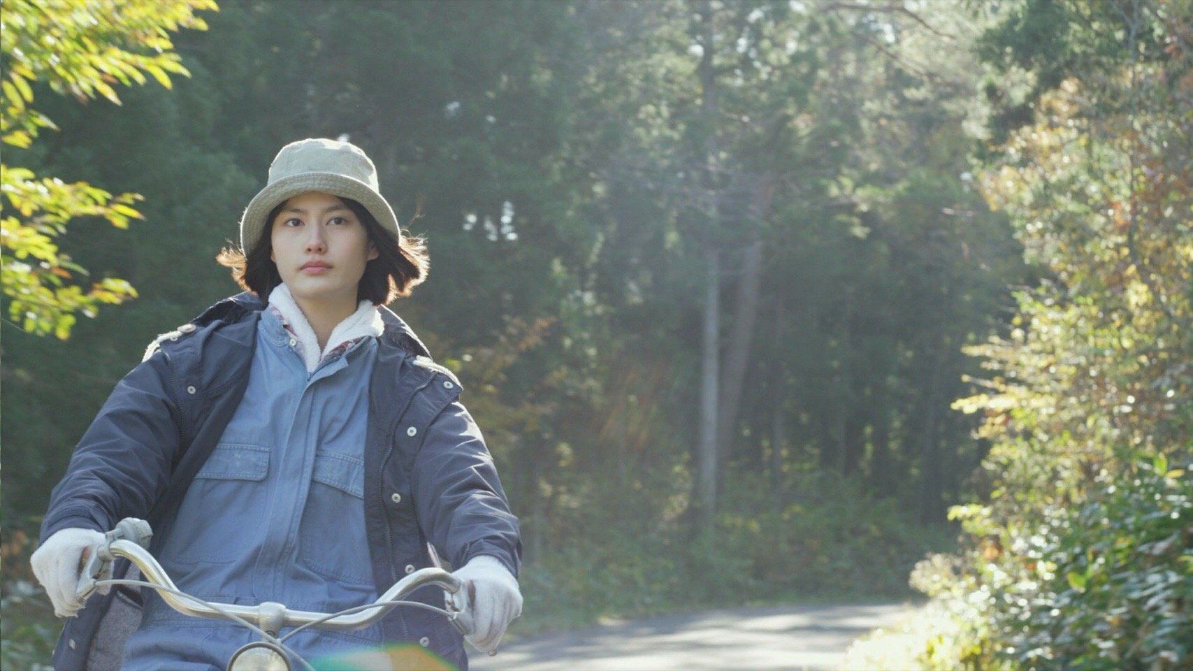 戴渔夫帽的女性在林间路上骑自行车